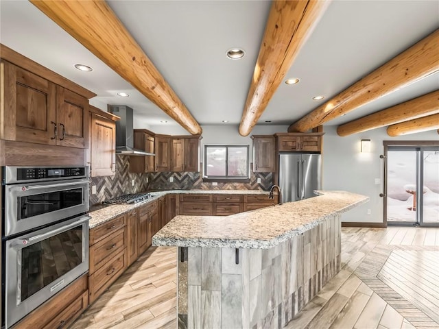 kitchen featuring wall chimney exhaust hood, a kitchen bar, appliances with stainless steel finishes, a kitchen island with sink, and backsplash