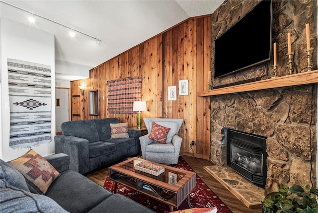 living area featuring wooden walls, vaulted ceiling, a stone fireplace, wood finished floors, and a textured ceiling