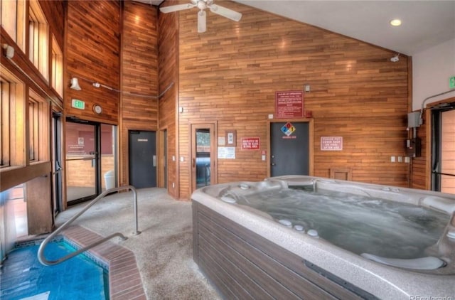 miscellaneous room with a hot tub, ceiling fan, light colored carpet, wood walls, and high vaulted ceiling