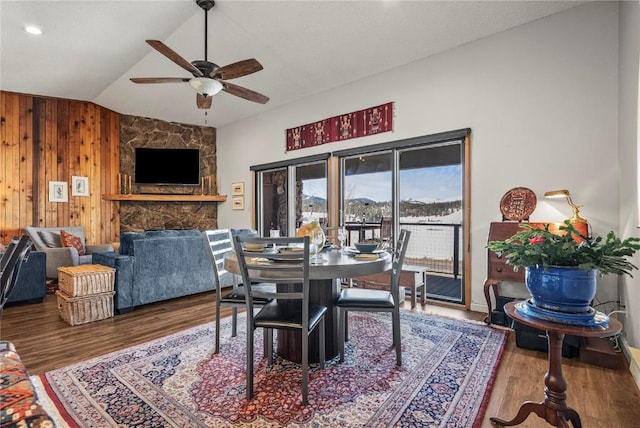 dining space featuring vaulted ceiling, wooden walls, wood finished floors, and a ceiling fan