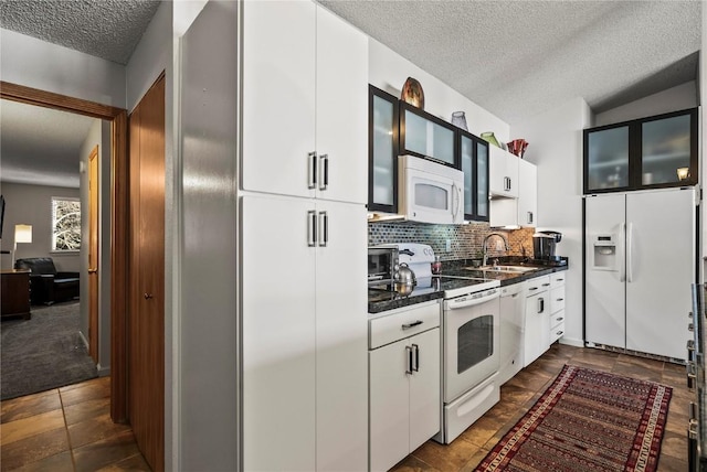 kitchen featuring dark countertops, glass insert cabinets, decorative backsplash, white appliances, and a sink