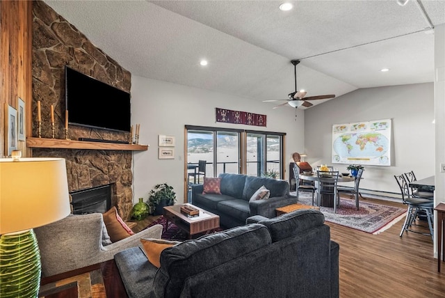 living area featuring wood finished floors, ceiling fan, a stone fireplace, vaulted ceiling, and a textured ceiling