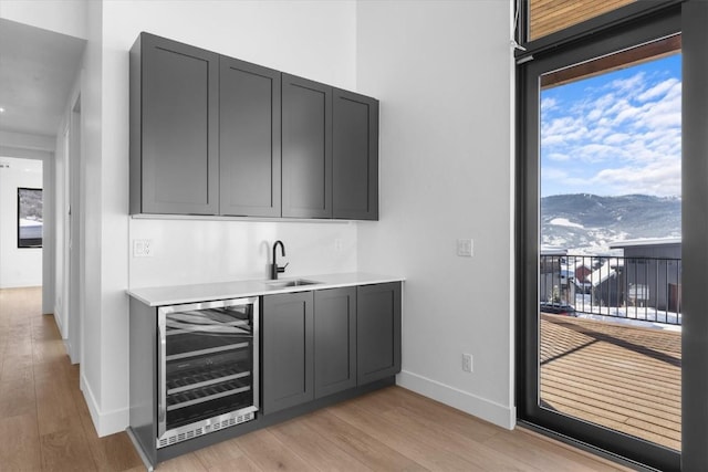 bar with light hardwood / wood-style floors, beverage cooler, a mountain view, and sink