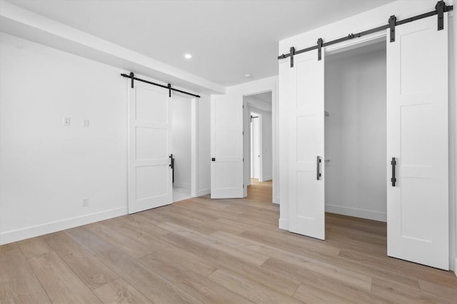 unfurnished bedroom featuring light hardwood / wood-style floors and a barn door