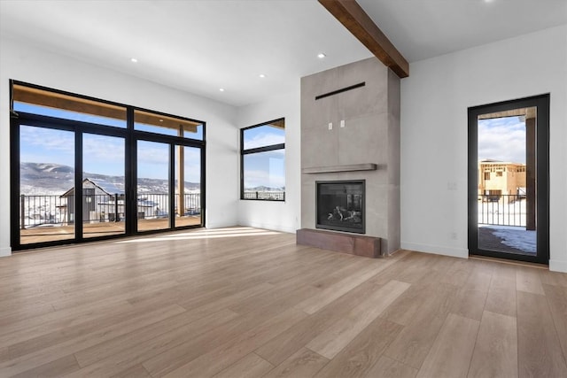 unfurnished living room with a mountain view, a large fireplace, beam ceiling, and light hardwood / wood-style flooring