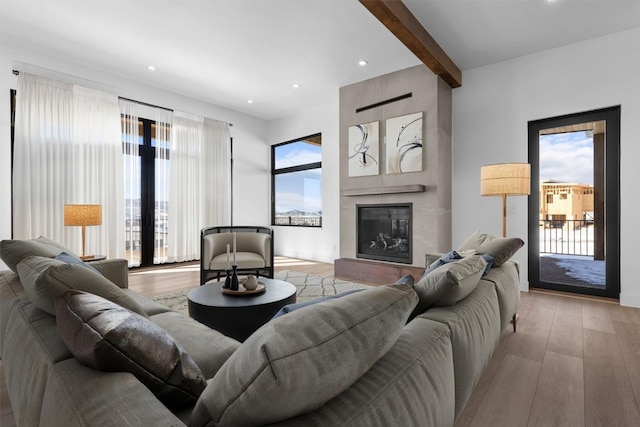 living room with beamed ceiling, a healthy amount of sunlight, a fireplace, and light wood-type flooring