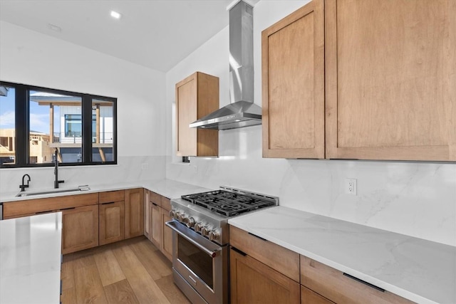 kitchen featuring high end stainless steel range, sink, light stone countertops, light hardwood / wood-style floors, and wall chimney range hood