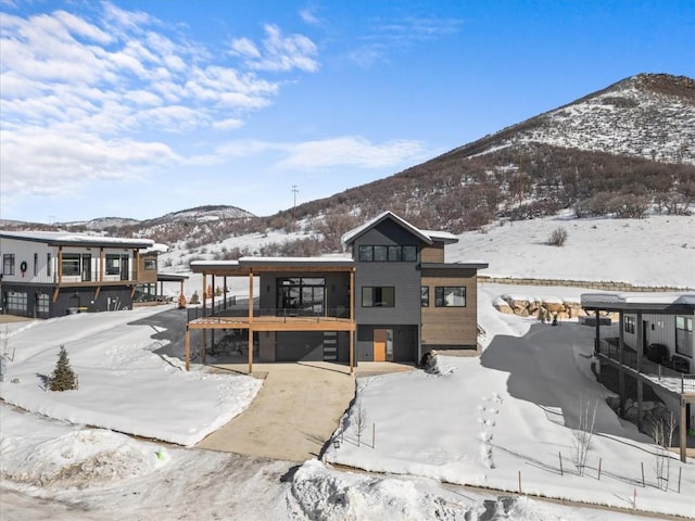 snow covered rear of property featuring a garage and a deck with mountain view