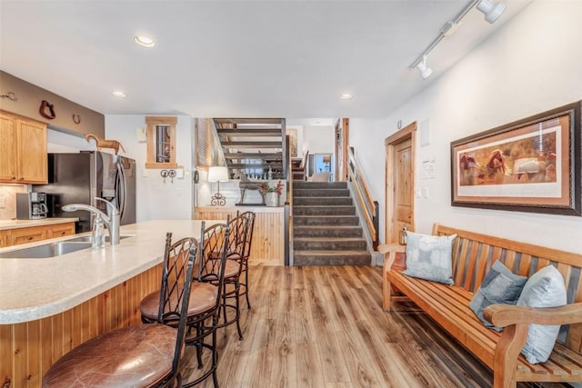 kitchen featuring sink, stainless steel refrigerator with ice dispenser, hardwood / wood-style floors, track lighting, and a breakfast bar