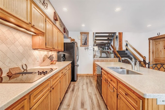 kitchen with appliances with stainless steel finishes, backsplash, a kitchen island with sink, sink, and light hardwood / wood-style flooring