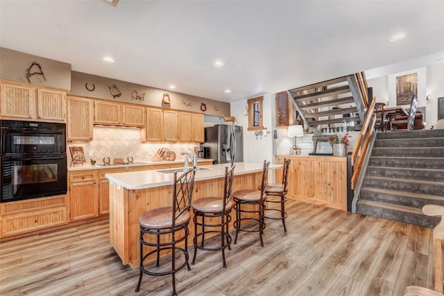 kitchen with decorative backsplash, sink, black appliances, light hardwood / wood-style flooring, and an island with sink