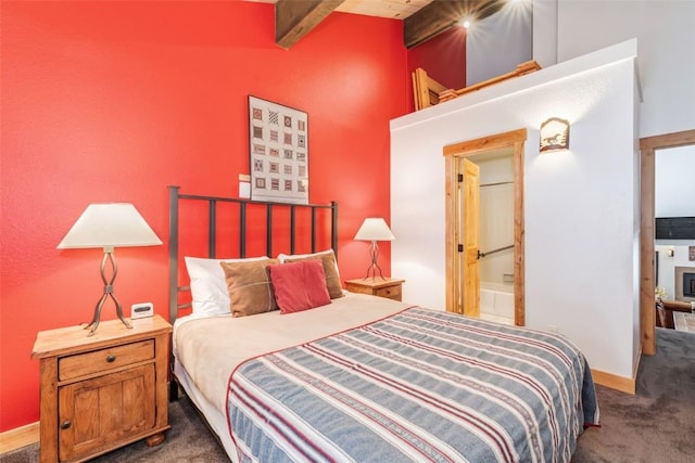 bedroom with dark colored carpet, beam ceiling, and connected bathroom