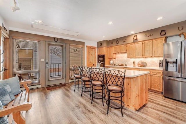 kitchen with stainless steel fridge with ice dispenser, light hardwood / wood-style flooring, decorative backsplash, light brown cabinetry, and a center island with sink