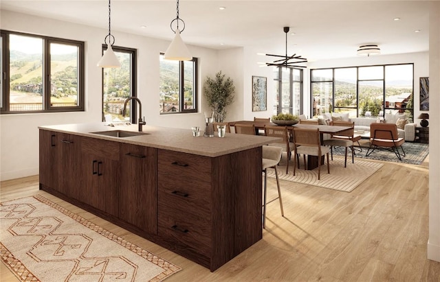 kitchen featuring decorative light fixtures, a center island with sink, dark brown cabinets, and sink