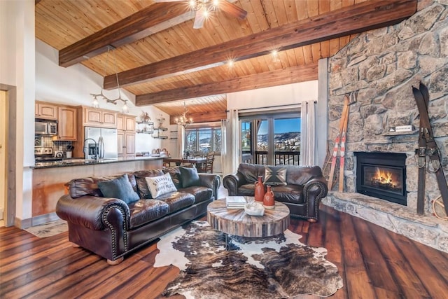 living room with dark wood-type flooring, ceiling fan with notable chandelier, a stone fireplace, vaulted ceiling with beams, and wood ceiling