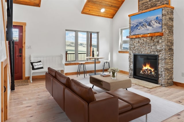 living room with light wood-style floors, baseboards, high vaulted ceiling, and a stone fireplace