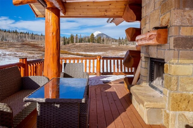 snow covered deck with a mountain view and an outdoor stone fireplace