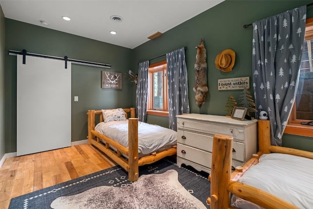 bedroom with a barn door and light hardwood / wood-style flooring