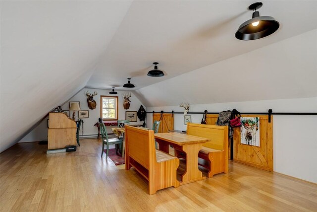 bonus room with a barn door, light hardwood / wood-style floors, and vaulted ceiling