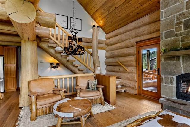 living area featuring high vaulted ceiling, a stone fireplace, rustic walls, light hardwood / wood-style floors, and a chandelier