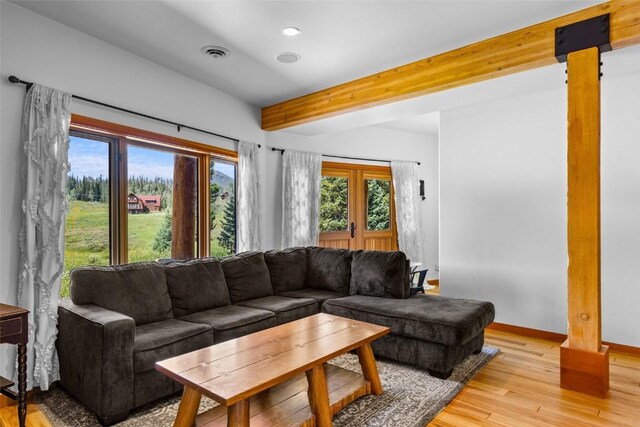 living room with beam ceiling, light hardwood / wood-style flooring, and french doors