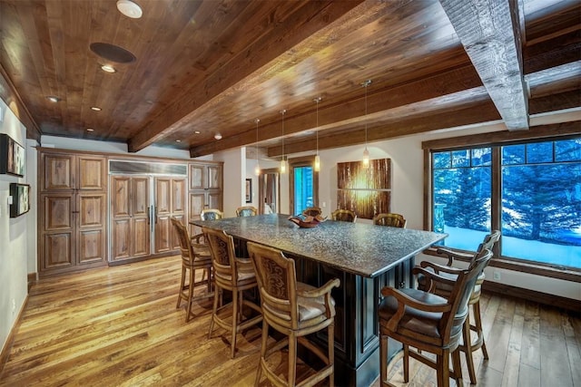 kitchen featuring a kitchen bar, decorative light fixtures, light hardwood / wood-style flooring, dark stone countertops, and beamed ceiling