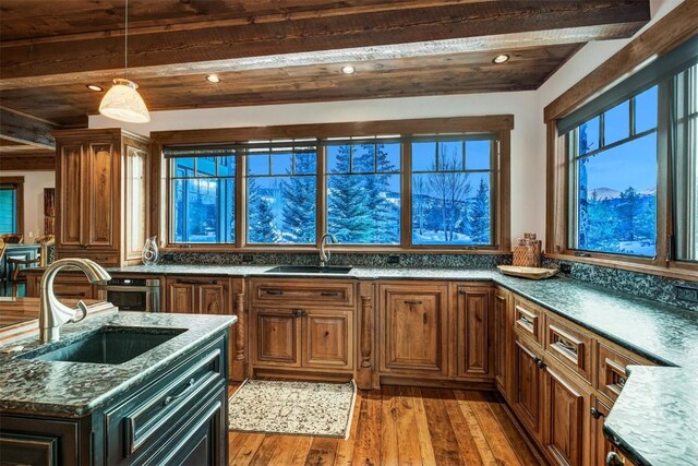 kitchen with beamed ceiling, dark hardwood / wood-style floors, dark stone counters, and sink