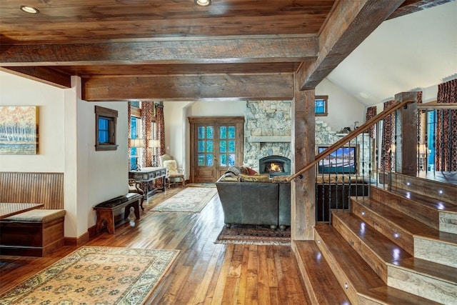 living room featuring beamed ceiling, a stone fireplace, wood ceiling, and hardwood / wood-style floors