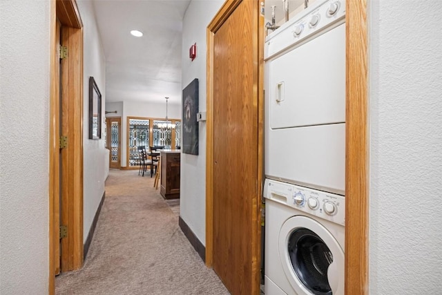 laundry room featuring stacked washer / drying machine, light carpet, and an inviting chandelier