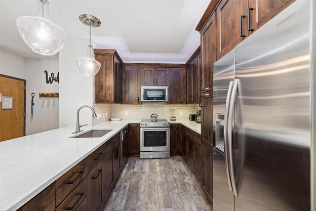 kitchen featuring sink, tasteful backsplash, decorative light fixtures, appliances with stainless steel finishes, and hardwood / wood-style flooring