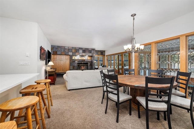 dining space featuring a large fireplace, light colored carpet, and a notable chandelier