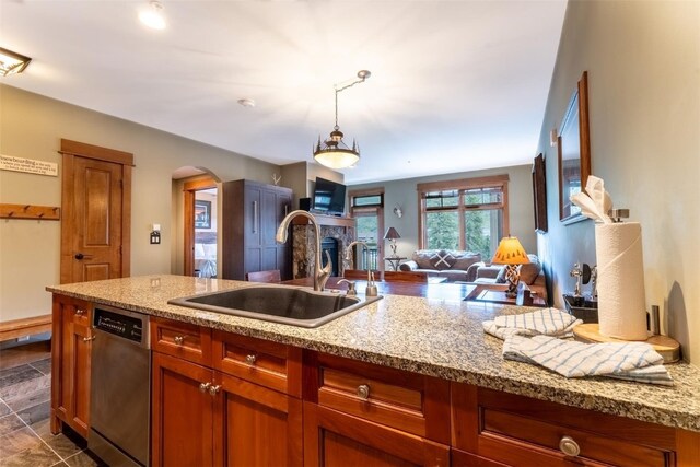 kitchen with dishwasher, a stone fireplace, sink, hanging light fixtures, and light stone counters