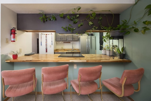 kitchen featuring stainless steel refrigerator, sink, wooden counters, kitchen peninsula, and black electric stovetop