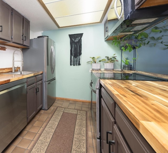 kitchen featuring sink, light tile patterned flooring, stainless steel appliances, and wood counters