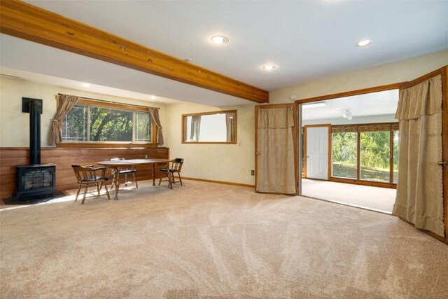 dining space with beamed ceiling, a wood stove, and carpet flooring