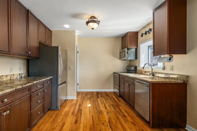 kitchen with dark stone countertops, sink, stainless steel appliances, and light hardwood / wood-style flooring