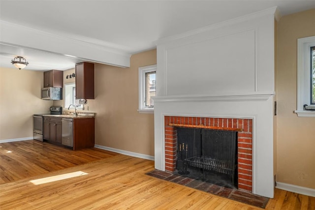 unfurnished living room featuring crown molding, sink, light wood-type flooring, and a brick fireplace