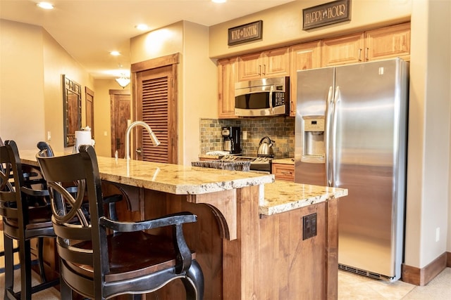 kitchen with a center island with sink, a kitchen breakfast bar, appliances with stainless steel finishes, tasteful backsplash, and light stone counters