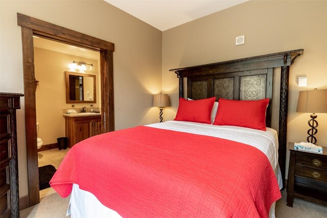 bedroom with ensuite bathroom, sink, and light carpet