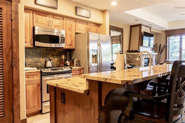 kitchen featuring light stone countertops, tasteful backsplash, a kitchen breakfast bar, a center island with sink, and appliances with stainless steel finishes