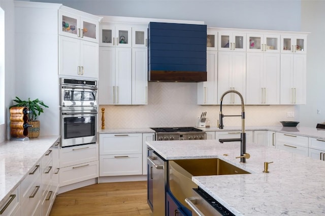 kitchen featuring stainless steel appliances, glass insert cabinets, white cabinets, and light stone counters