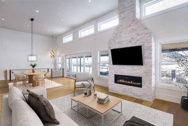 living area with baseboards, a high ceiling, a fireplace, and light wood finished floors