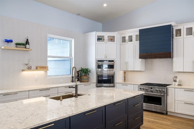 kitchen with custom exhaust hood, white cabinetry, stainless steel appliances, sink, and light wood-type flooring