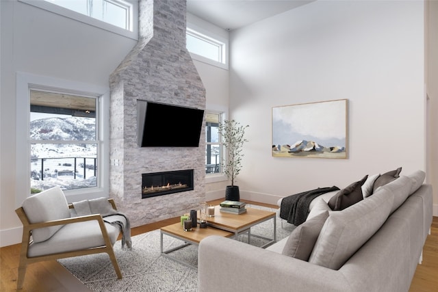 living area featuring baseboards, a fireplace, a towering ceiling, and light wood-style floors