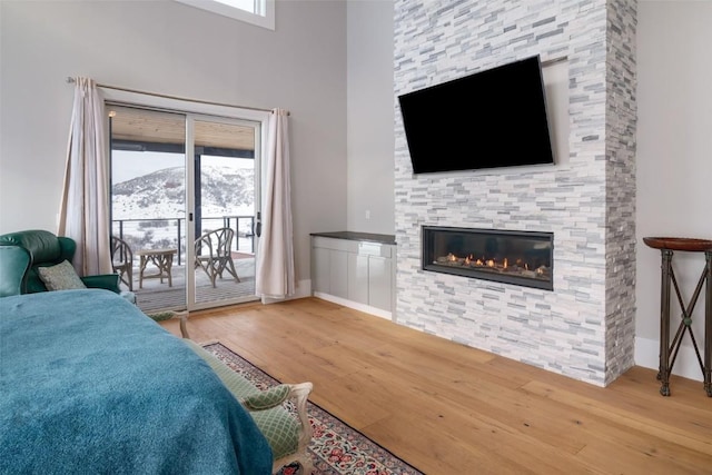 bedroom with access to outside, a stone fireplace, and hardwood / wood-style flooring