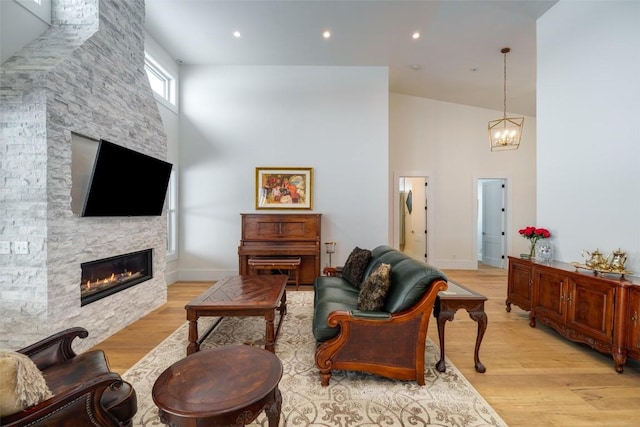 living room featuring an inviting chandelier, light hardwood / wood-style floors, a fireplace, and a high ceiling