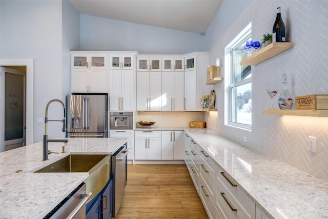 kitchen with open shelves, appliances with stainless steel finishes, glass insert cabinets, white cabinetry, and light stone countertops