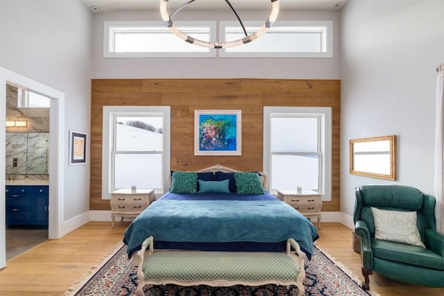 bedroom with connected bathroom, light hardwood / wood-style floors, a towering ceiling, and multiple windows