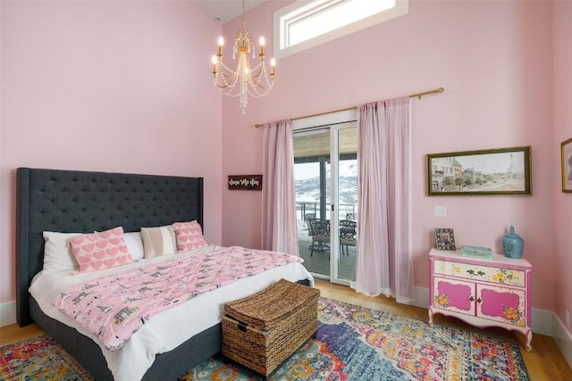 bedroom with access to outside, wood finished floors, multiple windows, and an inviting chandelier