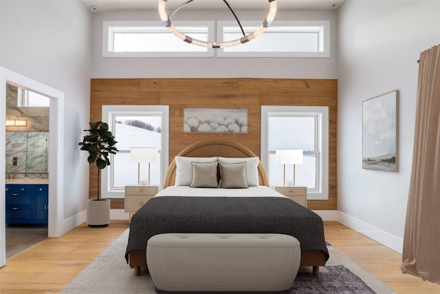 bedroom featuring baseboards, connected bathroom, light wood-style flooring, and a towering ceiling